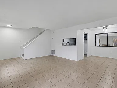 Open tiled living room with staircase and kitchen pass-through
